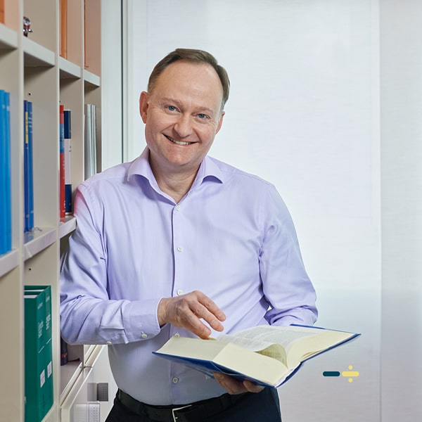 Rolf Masdorp steht mit einem Stift in der Hand vor einem Whiteboard und lächelt in die Kamera